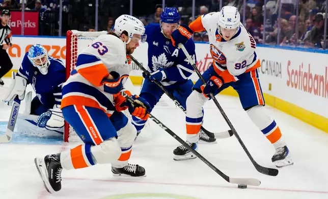 New York Islanders' Matias MacCelli (63) moves the puck as New York Islanders' Simon Holmstrom (92) and Toronto Maple Leafs' Morgan Rielly (44) look on during the first period of an NHL hockey game in Toronto, Saturday, Oct. 17, 2026. (Frank Gunn/The Canadian Press via AP)
