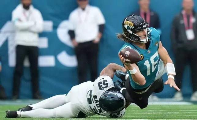 Jacksonville Jaguars quarterback Trevor Lawrence (16) passes as he's tackled by Philadelphia Eagles linebacker Zack Baun (53) during an NFL football game in London, Sunday, Oct. 11, 2026. (AP Photo/Alastair Grant)