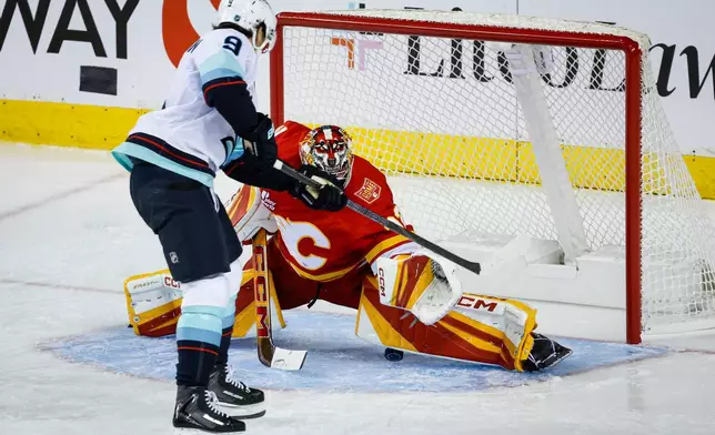 Seattle Kraken's Chandler Stephenson, left, scores against Calgary Flames goalie Dustin Wolf, right, during the third period of an NHL hockey game in Calgary, Alberta, Thursday, Oct. 1, 2026.(Jeff McIntosh/The Canadian Press via AP)