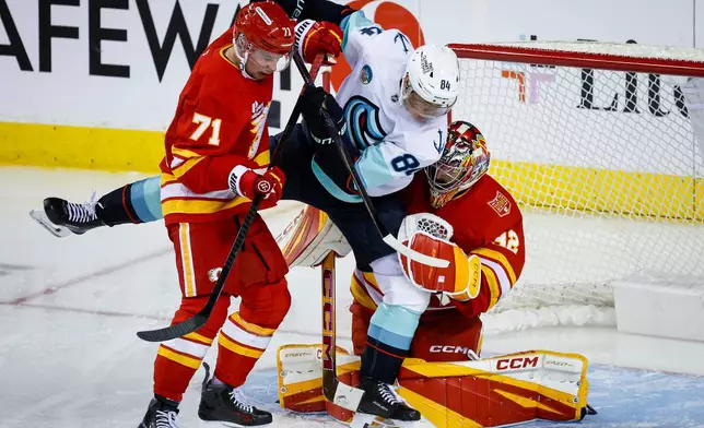 Seattle Kraken's Kaapo Kakko, centre, is checked by Calgary Flames' Simon Nemec, left, into goalie Dustin Wolf during the third period of an NHL hockey game in Calgary, Thursday, Oct. 1, 2026. (Jeff McIntosh/The Canadian Press via AP)