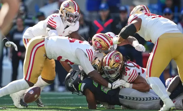 Seattle Seahawks running back Emanuel Wilson, bottom, fumbles the ball before San Francisco 49ers recovered the ball during the first half of an NFL football game Sunday, Oct. 11, 2026, in Seattle. (AP Photo/Lindsey Wasson)