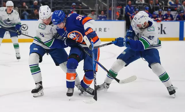 New York Islanders' Victor Eklund (38) fights for control of the puck with with Vancouver Canucks' Tom Willander (5) and Max Sasson (63) during the second period of an NHL hockey game Tuesday, Oct. 13, 2026, in Elmont, N.Y. (AP Photo/Frank Franklin II)