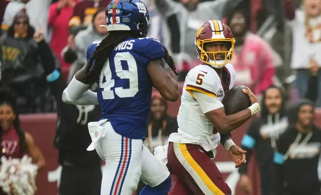 Washington Commanders quarterback Jayden Daniels (5) looks at New York Giants linebacker Tremaine Edmunds (49) as he scores a touchdown during the second half of an NFL football game in Landover, Md., Sunday, Oct. 11, 2026. (AP Photo/Stephanie Scarbrough)