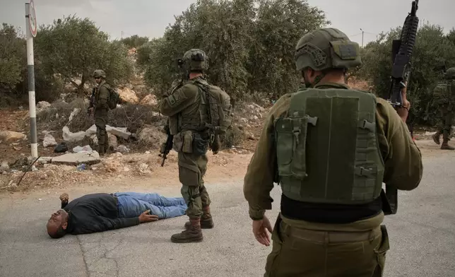 Israeli soldiers stand beside a wounded Palestinian man lying on a road after soldiers shot him following a settler attack on Palestinians harvesting olives in the occupied West Bank village of Abu Falah, Friday, Oct. 16, 2026. (AP Photo/Leo Correa)
