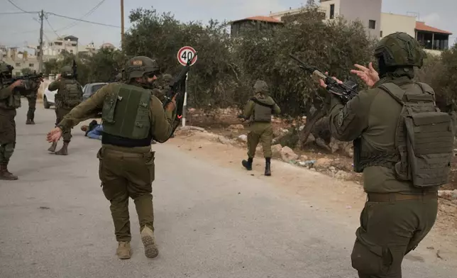 Israeli soldiers move toward a Palestinian man lying wounded on a road after they shot him following a settler attack on Palestinians harvesting olives in the West Bank village of Abu Falah, Friday, Oct. 16, 2026. (AP Photo/Leo Correa)