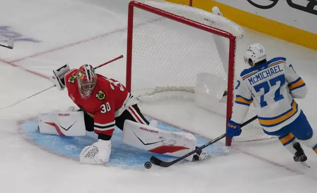Chicago Blackhawks goaltender Spencer Knight, left, makes a save on St. Louis Blues left wing Connor McMichael, right, during the first period of an NHL hockey game, Tuesday, Oct. 6, 2026, in Chicago. (AP Photo/David Banks)