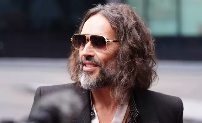 Russell Brand speaks to the media as he arrives at Southwark Crown Court in London, Wednesday Oct. 14, 2026. (Ben Whitley/PA via AP)