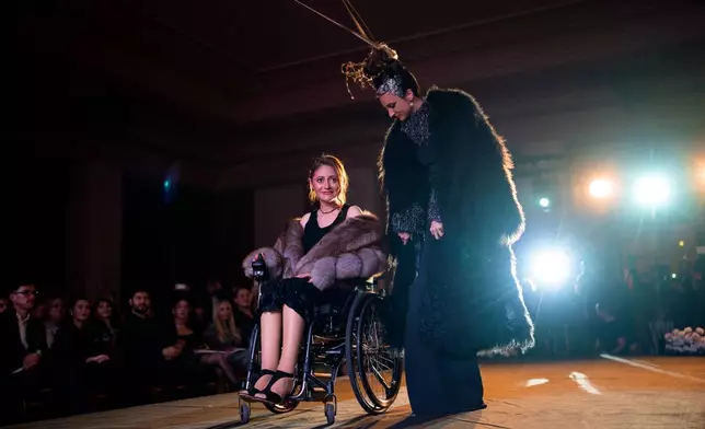 Ana Mihaela Stancu, a wheelchair user, is accompanied by a model during the Atypic Beauty Gala fashion show, an event promoting inclusion and equal opportunities for people with disabilities, in Bucharest, Romania, Thursday, Oct. 22, 2026. (AP Photo/Andreea Alexandru)