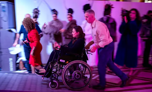 A man assists a wheelchair using model on a ramp to the catwalk during the Atypic Beauty Gala fashion show, an event promoting inclusion and equal opportunities for people with disabilities, in Bucharest, Romania, Thursday, Oct. 22, 2026. (AP Photo/Andreea Alexandru)