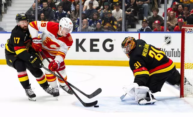 Calgary Flames' Samuel Honzek (29) attempts to shoot against Vancouver Canucks goalie Leevi Merilainen (31) as Canucks' Filip Hronek (17) defends during the first period of an NHL hockey game in Vancouver, British Columbia, Saturday, Oct. 3, 2026. (Jacob Mallari/The Canadian Press via AP)