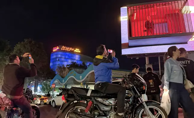 People take pictures of a billboard installation featuring an actor portraying President Donald Trump behind bars in a mock prison cell in Tajrish Square in Tehran, Wednesday, Oct. 21, 2026. (AP Photo/Vahid Salemi)