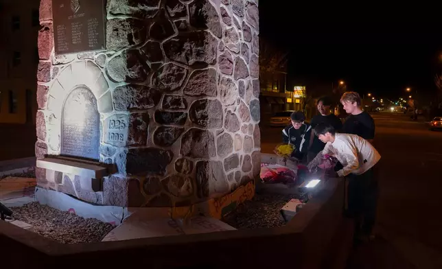 A group of young men pay their respects to the victims of a grass fire that killed four soldiers at Canadian Forces Base Wainwright, at the Memorial Clock Tower in Wainwright, Alberta, on Sunday, Oct. 18, 2026. (John Ulan/The Canadian Press via AP)