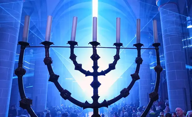 People admire a light installation behind the early medieval seven-branched candelabrum, dating from around the year 1000, during a light festival at the Cathedral in Essen, Germany, Tuesday, Oct. 6, 2026. (AP Photo/Martin Meissner)