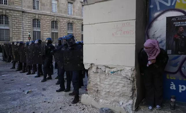 A protester watches riot police next to a tag reading 'Police kill our children' during a demonstration against rising living costs, joining students' grievances, in Paris, Saturday, Oct. 17, 2026. (AP Photo/Thibault Camus)