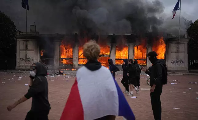 A protester wraps a French flag around them in front of the burning tourism office during a demonstration against rising living costs and in solidarity with students’ grievances in Lyon, France, Saturday, Oct. 17, 2026.(AP Photo/Laurent Cipriani)