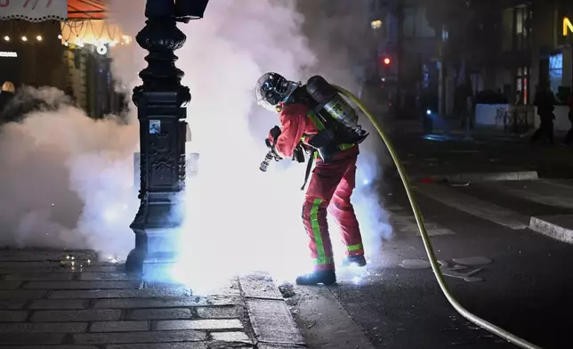 A firefighter extinguishes a fire during clashes between protestors and police in Paris, Sunday, Oct. 18, 2026. (AP Photo/Emma Da Silva)