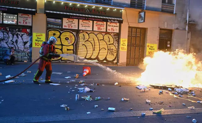 A firefighter extinguishes a fire during clashes with police a day after a demonstration against rising living costs, joining students' grievances, in Paris, Sunday, Oct. 18, 2026. (AP Photo/Emma Da Silva)