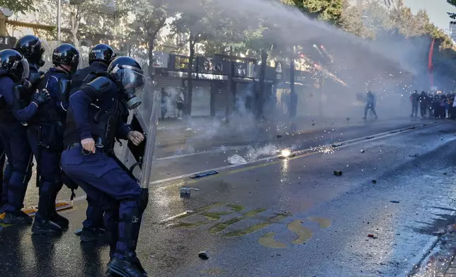 Riot police take cover behind their shields as fireworks explode nearby and a water cannon sprays protesters during an anti-government protest in Tirana, Albania, Tuesday, Oct. 20, 2026. (AP Photo/Boris Grdanoski)