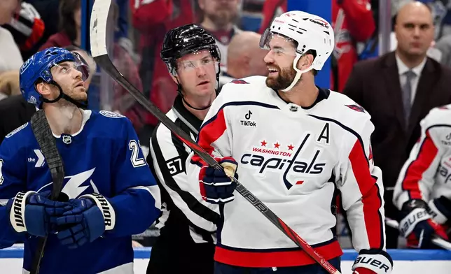 Washington Capitals right wing Tom Wilson (43) laughs as linesman Dylan Blujus (57) separates him from the Tampa Bay Lightning bench area during the second period of an NHL hockey game Saturday, Oct. 3, 2026, in Tampa, Fla. (AP Photo/Jason Behnken)