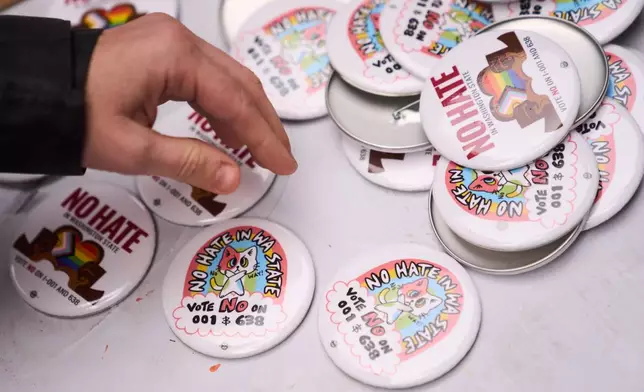 A person picks up a button during a "No Hate in WA State" rally against multiple initiatives on the November ballot, including Washington State Initiative 638, which would prohibit transgender girls from competing in girls' sports, Saturday, Oct. 17, 2026, in Seattle. (AP Photo/Lindsey Wasson)