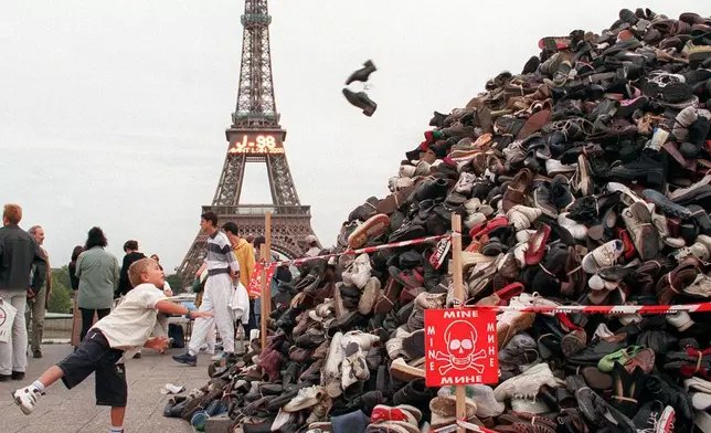 FILE - A child throws a pair of shoes onto a pile of footwear as part of a symbolic demonstration against anti-personnel mines, in Paris, Saturday, Sept. 25, 1999, with the Eiffel Tower in the background. (AP Photo/Francois Mori, File)