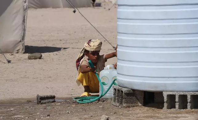 A displaced Yemeni boy fills water containers from a storage tank at the Al-Fardous displacement camp in Ras Imran, on the outskirts of Aden, Yemen, Sunday, Oct. 25, 2026. (AP Photo/Abdulnasser Alseddik)