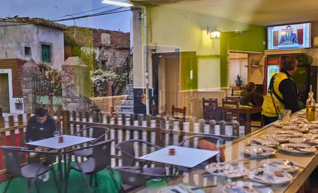 People seen through a window inside a bar in La Cabrera, on the outskirts of Madrid, Spain, watch a televised speech by Spanish Prime Minister Pedro Sanchez from La Moncloa Palace announcing national elections, Monday, Oct. 5, 2026. (AP Photo/Bernat Armangue)