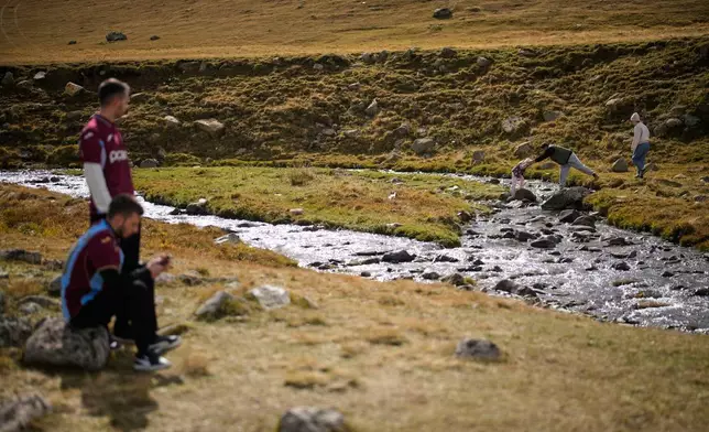 Trabzonspor fans attempt to cross a stream to reach the rock where the club's Egyptian soccer player Mohamed Salah previously posed for a photo he shared on social media, in Trabzon province, along Turkey's Black Sea coast, Monday, Oct. 19, 2026. (AP Photo/Khalil Hamra)