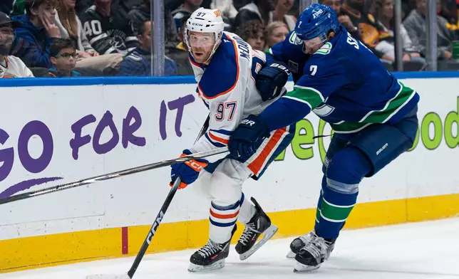 Vancouver Canucks' Luke Schenn (2) tries to check Edmonton Oilers' Connor McDavid (97) during second period NHL hockey action in Vancouver, B.C., on Thursday, Oct. 1, 2026. (Rich Lam/The Canadian Press via AP)