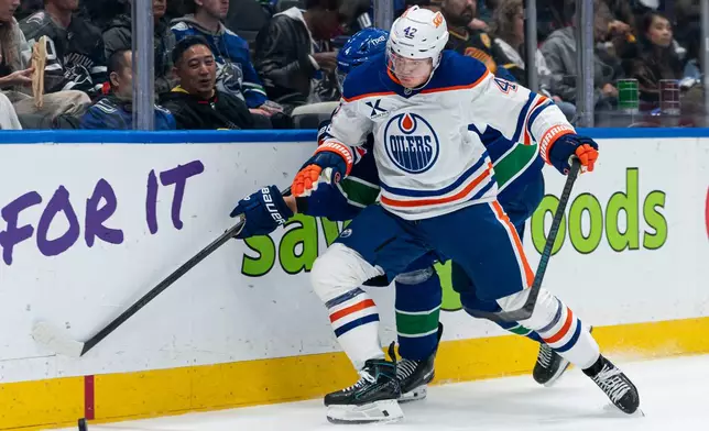 Edmonton Oilers' Kasperi Kapanen (42) battles with Vancouver Canucks' Jamie Oleksiak (4) for the puck during second period NHL hockey action in Vancouver, B.C., on Thursday, Oct. 1, 2026. (Rich Lam/The Canadian Press via AP)