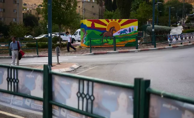 People walk near a bomb shelter and elections campaign banners in Kiryat Shmona, Israel's largest northern city near Lebanon's border, ahead of the country's general, Tuesday, Oct. 13, 2026. (AP Photo/Ariel Schalit)