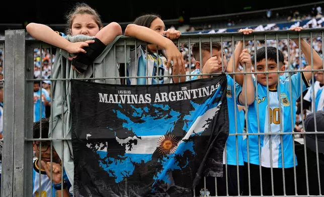 Fans stand beside a banner reading in Spanish, "The Malvinas are Argentine," referring to the Falkland Islands, before Lionel Messi's final match for Argentina, an international friendly against Benin in Buenos Aires, Tuesday, Oct. 6, 2026. (AP Photo/Natacha Pisarenko)