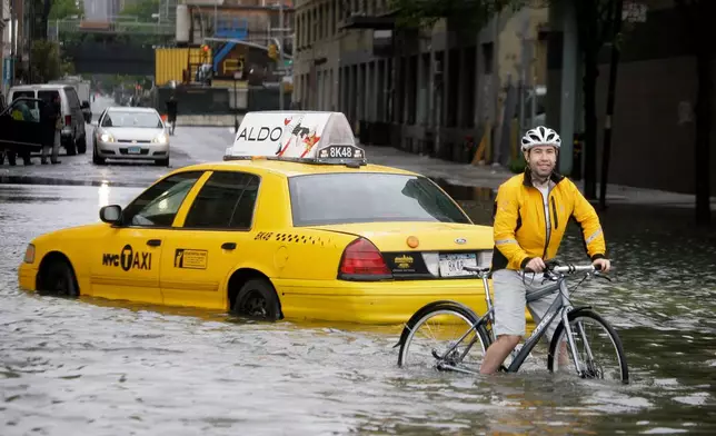 FILE - A bicyclist making his way past a stranded taxi on a flooded New York City street as Tropical Storm Irene passes through on Aug. 28, 2011. (AP Photo/Peter Morgan, File)