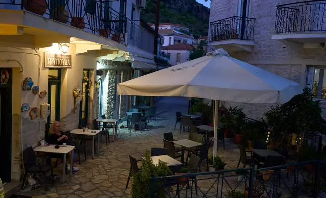 A woman drinks coffee at a snack bar on the island of Kalamos in the Ionian Sea, western Greece, Wednesday, Sept. 23, 2026. (AP Photo/Petros Giannakouris)