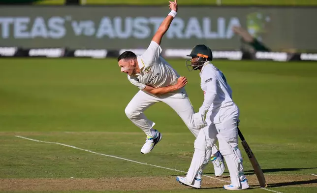 Australia's Scott Boland, left, bowls as South Africa's captain Temba Bavuma, looks on on day two of the second cricket test match between South Africa and Australia, in Gqeberha, South Africa, Monday, Oct. 19, 2026. (AP Photo/Themba Hadebe)