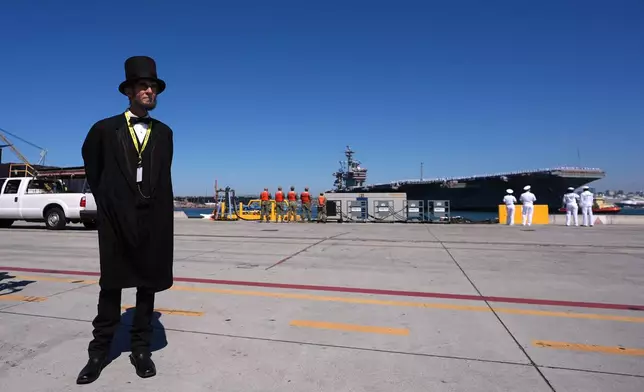 A man dressed as Abraham Lincoln stands nearby as the USS Abraham Lincoln aircraft carrier returns to Naval Air Station North Island after deployment Thursday, Oct. 8, 2026, in Coronado, Calif. (AP Photo/Gregory Bull)