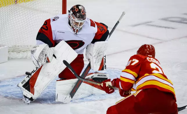 Carolina Hurricanes' goalie Brandon Bussi, left, deflects a shot from Calgary Flames' Matt Coronato during the third period of an NHL hockey game in Calgary, Alberta, Sunday, Oct. 18, 2026. (Jeff McIntosh/The Canadian Press via AP)