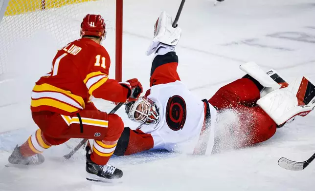 Carolina Hurricanes goalie Brandon Bussi, right, grabs the puck from Calgary Flames' Mikael Backlund (11) during the first period of an NHL hockey game in Calgary, Alberta, Sunday, Oct. 18, 2026. (Jeff McIntosh/The Canadian Press via AP)