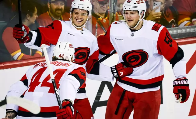 Carolina Hurricanes' Jesperi Kotkaniemi (82) celebrates after his goal with teammates Nicolas Deslauriers (44) and Eric Robinson, right, during the second period of an NHL hockey game in Calgary, Alberta, Sunday, Oct. 18, 2026. (Jeff McIntosh/The Canadian Press via AP)
