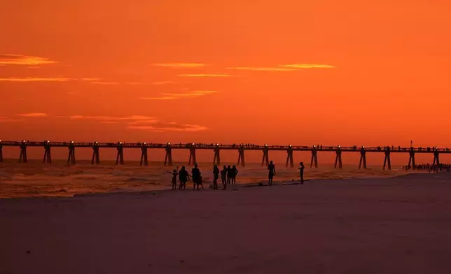 People walk on the beach at sunset as Hurricane Isaias approaches Pensacola Beach, Fla., Thursday, Oct. 8, 2026. (AP Photo/Gerald Herbert)