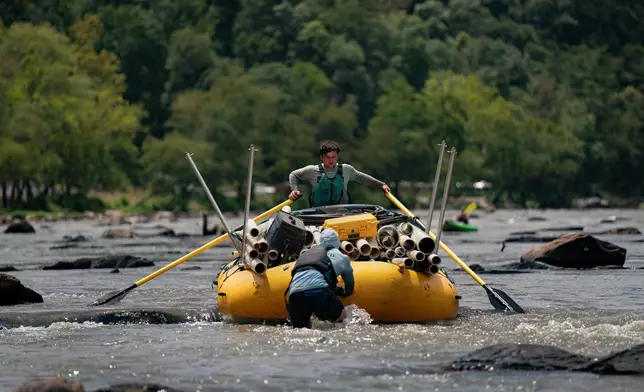 Workers from MountainTrue paddle IPEX PVC pipe they collected from the riverbank Wednesday, July 22, 2026, in Alexander, N.C. (AP Photo/Allison Joyce)