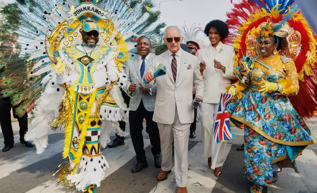 Britain's King Charles III shakes traditional cowbells as he parades with Junkanoo dancers flanked by Minister of Agriculture and Marine Resources Jomo Campbell, left, and Minister of Culture, Arts and Heritage Leslia Brice, right, during a cultural festival in Rawson Square, Nassau, Bahamas, Wednesday, Oct. 28, 2026. (AP Photo/Tim Aylen)