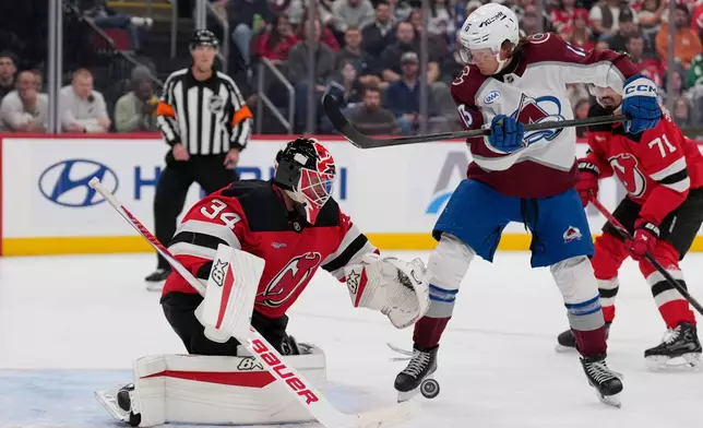 New Jersey Devils goaltender Jake Allen, left, defends the net while Colorado Avalanche's T.J. Hughes looks on during the third period of an NHL hockey game in Newark, N.J., Tuesday, Oct. 20, 2026. (AP Photo/Seth Wenig)