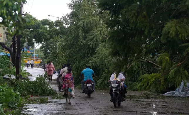 People walk past fallen trees at Kakinada, India, as Cyclone Arnab crossed the Andhra Pradesh coast in the early hours of Wednesday, Oct. 28, 2026. (AP Photo/Mahesh Kumar A.)