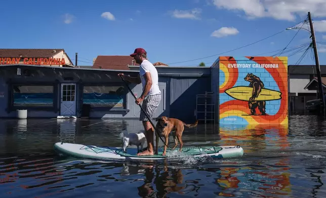 James Hays paddleboards with two dogs along a flooded section of Pacific Coast Highway in Huntington Beach, Calif., Wednesday, Oct. 28, 2026. (AP Photo/Jae C. Hong)