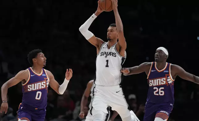 San Antonio Spurs forward Victor Wembanyama (1) is pressured by Phoenix Suns forward Ryan Dunn (0) and center Duop Reath (26) during the second half of a preseason NBA basketball game in San Antonio, Wednesday, Oct. 14, 2026. (AP Photo/Eric Gay)