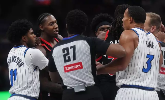 Referee Mitchell Ervin (27) gets between Toronto Raptors' RJ Barrett, second from left, and Orlando Magic's Desmond Bane (3) during the first half of an NBA Cup basketball game in Toronto, Friday, Oct. 30, 2026. (Nathan Denette/The Canadian Press via AP)