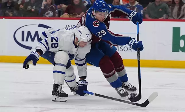 Colorado Avalanche center Nathan MacKinnon, right, shoots as Toronto Maple Leafs defenseman Troy Stecher, left, covers in the first period of an NHL hockey game Saturday, Oct. 10, 2026, in Denver. (AP Photo/David Zalubowski)