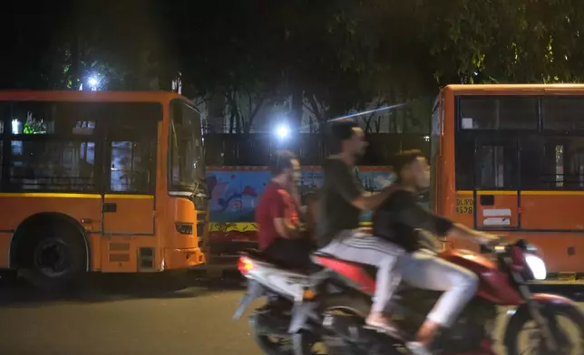 Riders drive past buses, used to carry protestors, in the heart of New Delhi, India, Monday, Oct. 12, 2026. (AP Photo/Yirmiyan Arthur)