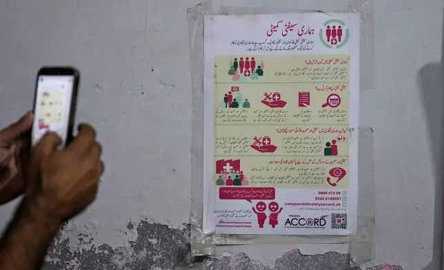 A man takes a photo of a poster with safety resources for factory workers at a Pakistan Institute of Labour Education & Research office in Karachi, Pakistan, Saturday, Oct. 3, 2026. (AP Photo/Anjum Naveed)